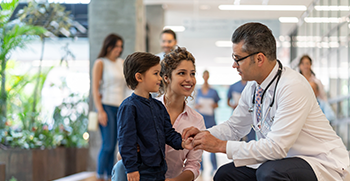 A doctor crouching to talk with a young child and mother